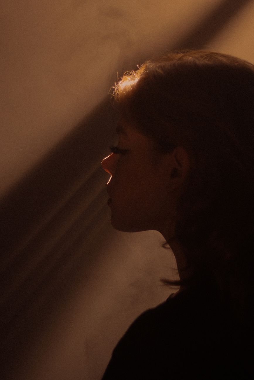 Side profile portrait of a woman in soft, dramatic lighting creating an artistic silhouette.